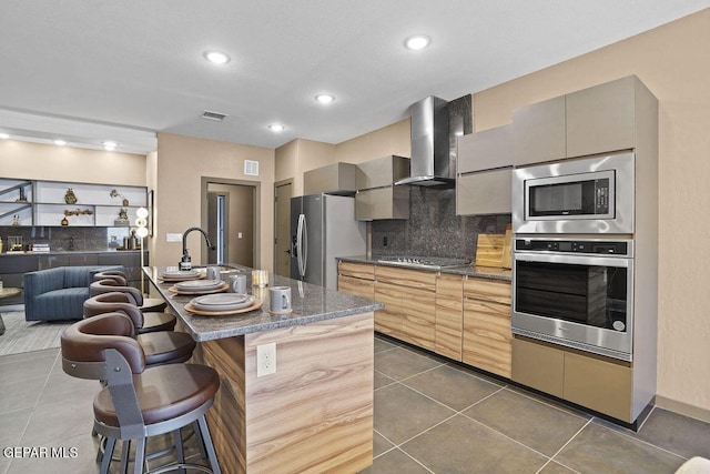 kitchen featuring a sink, appliances with stainless steel finishes, visible vents, a kitchen bar, and wall chimney exhaust hood