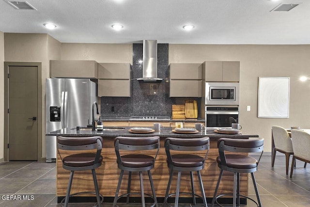 kitchen with decorative backsplash, stainless steel appliances, gray cabinetry, visible vents, and wall chimney exhaust hood