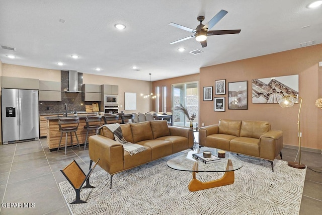 living room featuring light tile patterned flooring, visible vents, and ceiling fan with notable chandelier
