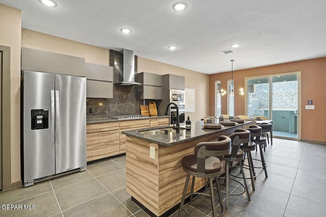 kitchen with a sink, stainless steel appliances, decorative backsplash, light tile patterned floors, and wall chimney range hood