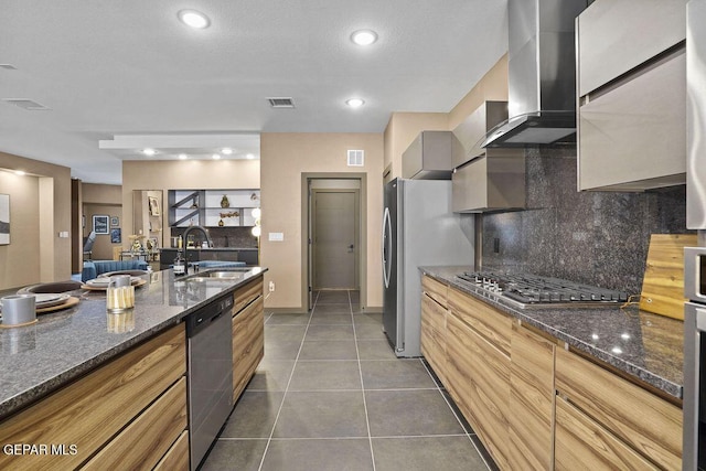 kitchen featuring a sink, decorative backsplash, stainless steel appliances, wall chimney exhaust hood, and visible vents