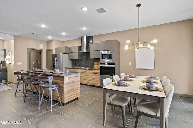 kitchen with tasteful backsplash, a kitchen island with sink, stainless steel appliances, wall chimney range hood, and visible vents
