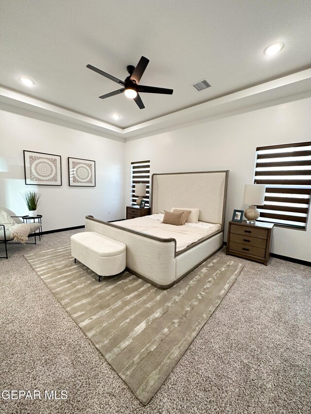 carpeted bedroom featuring recessed lighting, ceiling fan, baseboards, visible vents, and a tray ceiling