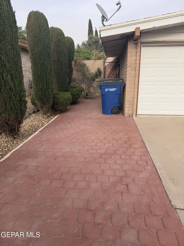 view of side of property with brick siding, driveway, fence, and a garage