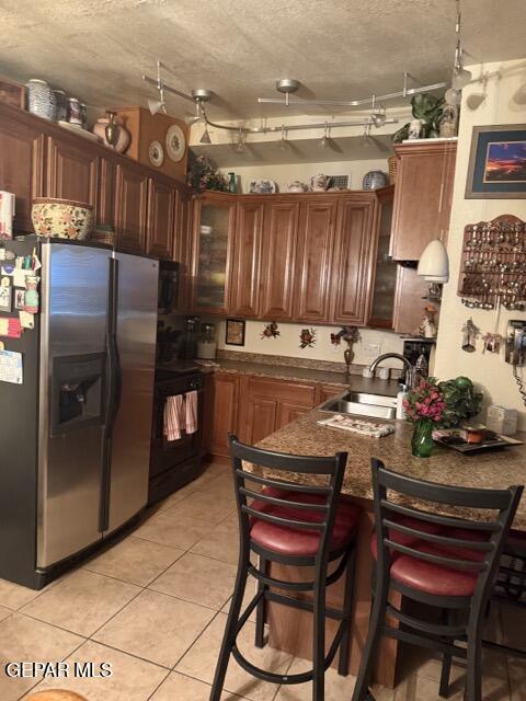kitchen with stainless steel fridge with ice dispenser, a peninsula, glass insert cabinets, black range with electric stovetop, and a sink