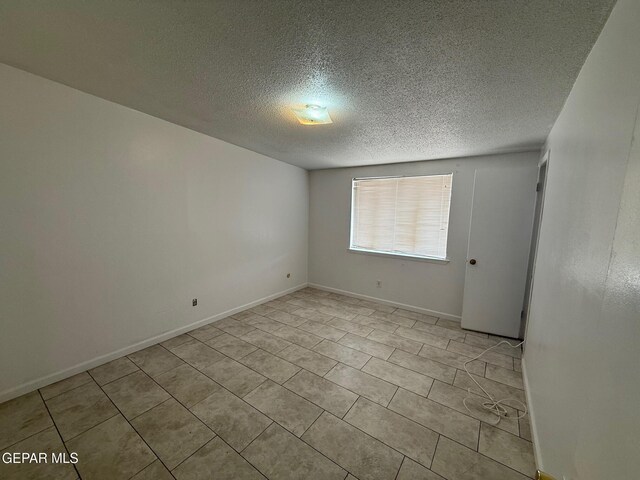 tiled empty room featuring a textured ceiling and baseboards