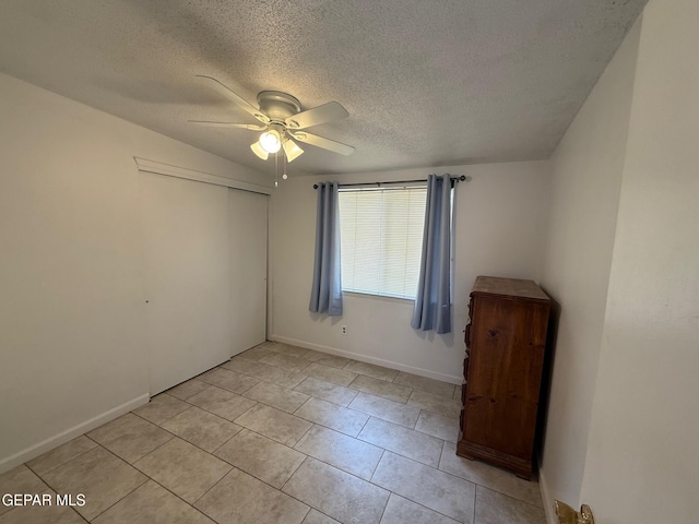 unfurnished bedroom featuring a textured ceiling, a closet, a ceiling fan, baseboards, and light tile patterned flooring