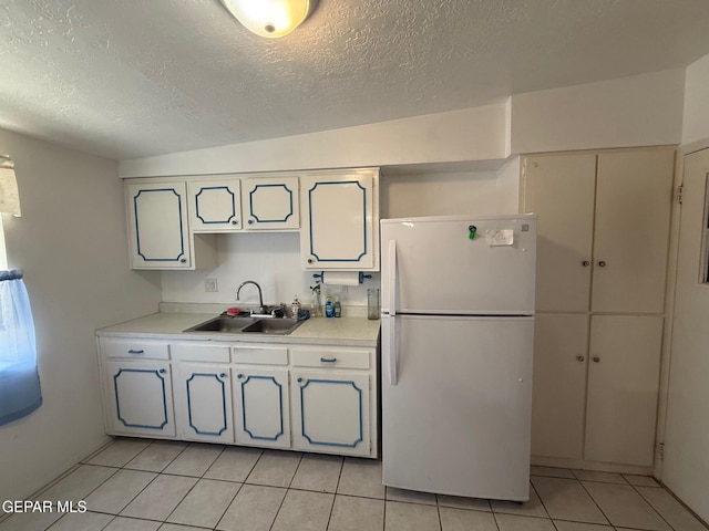 kitchen featuring freestanding refrigerator, a sink, a textured ceiling, light countertops, and light tile patterned flooring
