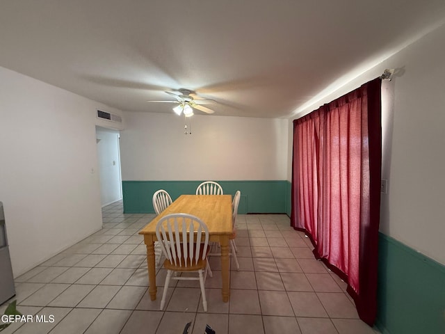 dining space featuring ceiling fan, light tile patterned floors, and wainscoting