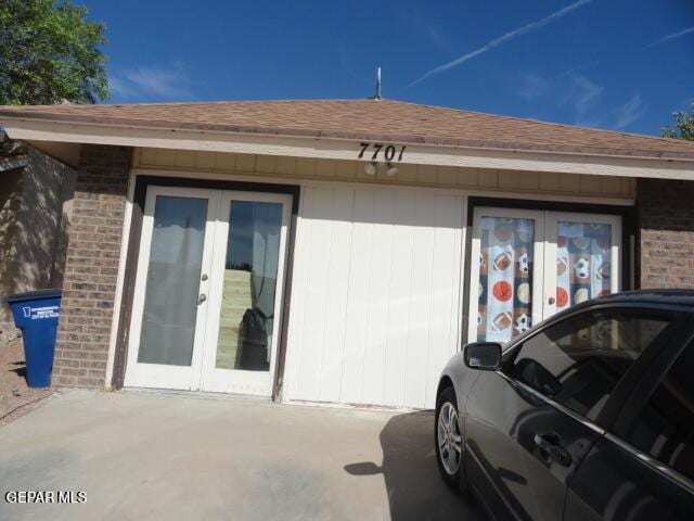 view of exterior entry featuring a shingled roof, french doors, and brick siding