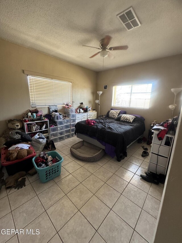 bedroom featuring light tile patterned flooring, a textured ceiling, visible vents, and a ceiling fan