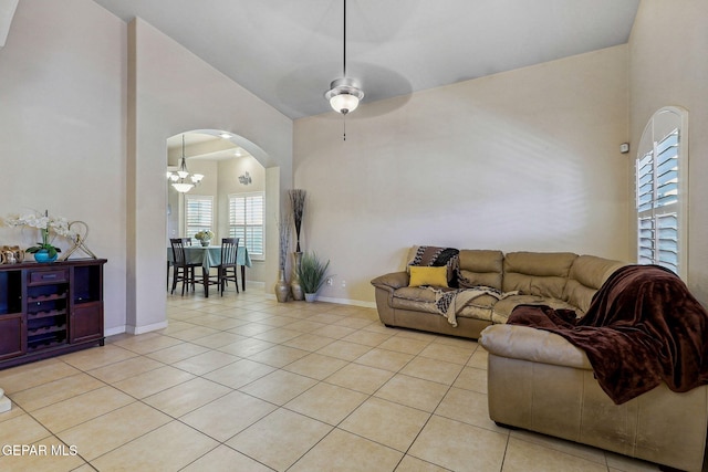 living area featuring arched walkways, ceiling fan, baseboards, high vaulted ceiling, and light tile patterned flooring