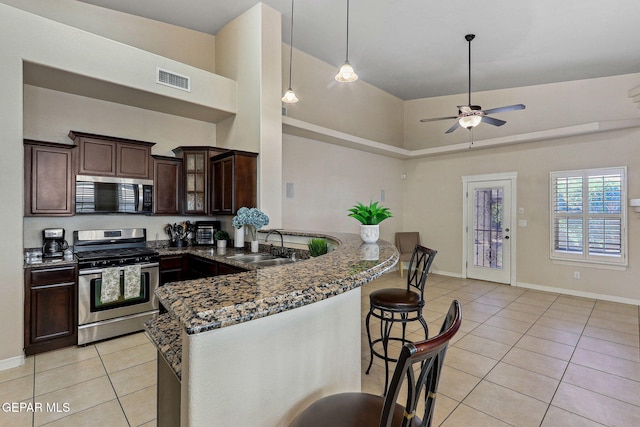 kitchen featuring dark stone countertops, light tile patterned floors, stainless steel appliances, a ceiling fan, and a peninsula