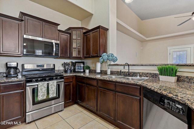kitchen with dark stone counters, a sink, stainless steel appliances, light tile patterned floors, and dark brown cabinets
