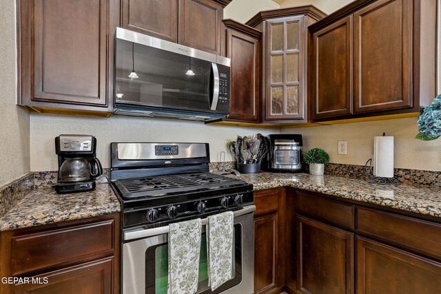 kitchen featuring stainless steel appliances, stone countertops, glass insert cabinets, and dark brown cabinets