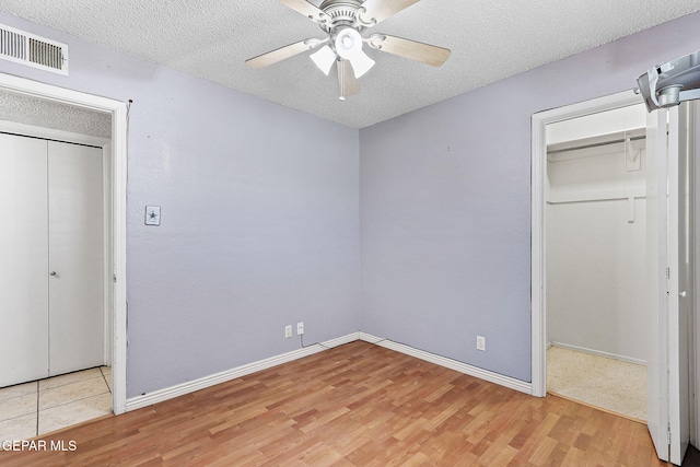 unfurnished bedroom featuring a textured ceiling, visible vents, baseboards, and light wood-style floors