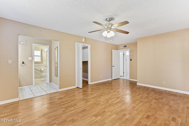 unfurnished room featuring a ceiling fan, a textured ceiling, visible vents, baseboards, and light wood finished floors