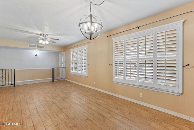 spare room featuring baseboards, visible vents, wood finished floors, and ceiling fan with notable chandelier