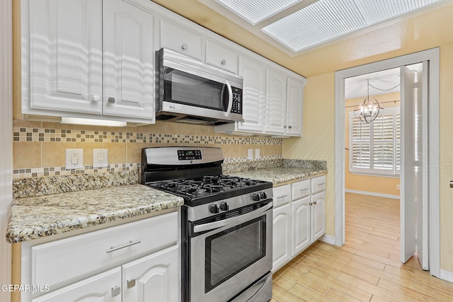 kitchen featuring an inviting chandelier, baseboards, white cabinets, appliances with stainless steel finishes, and backsplash
