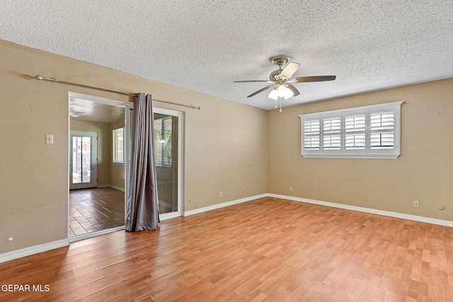 spare room with baseboards, a ceiling fan, light wood-style flooring, and a textured ceiling