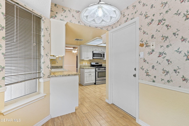 kitchen featuring a sink, appliances with stainless steel finishes, light wood finished floors, and wallpapered walls