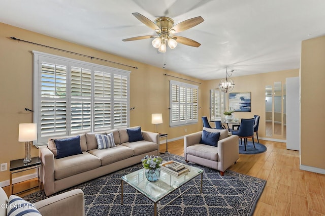 living room featuring baseboards, light wood finished floors, and ceiling fan with notable chandelier