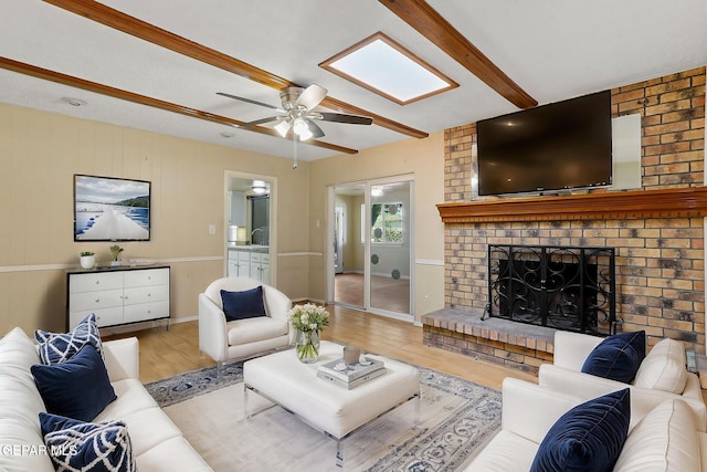 living room featuring a ceiling fan, wood finished floors, a fireplace, and beamed ceiling