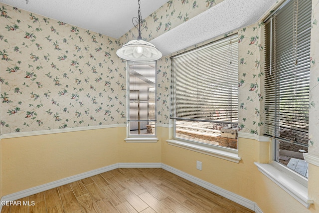 unfurnished dining area with baseboards, wallpapered walls, and a textured ceiling