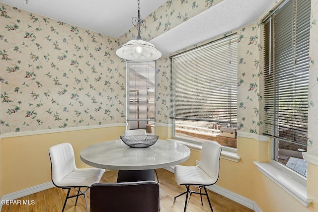 dining space featuring baseboards, wallpapered walls, and wood finished floors