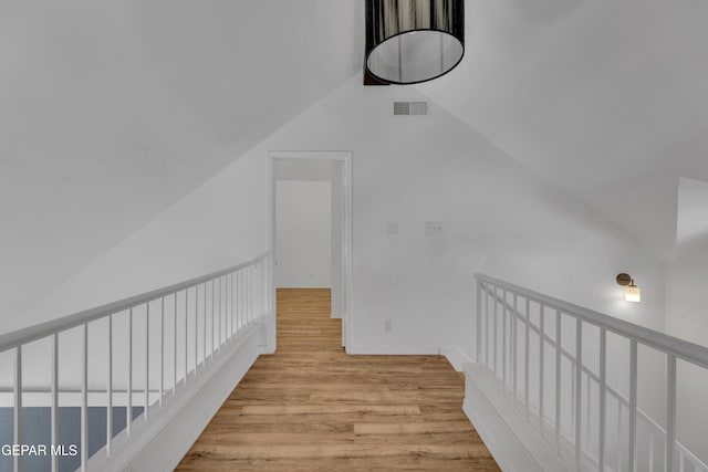hallway with lofted ceiling, visible vents, and wood finished floors