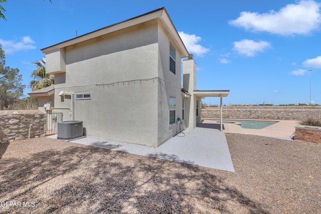 rear view of property with a patio, stucco siding, a fenced in pool, and central AC unit