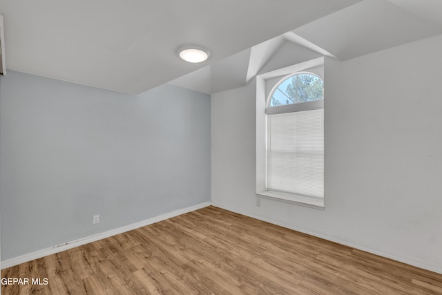 spare room featuring baseboards, vaulted ceiling, and wood finished floors