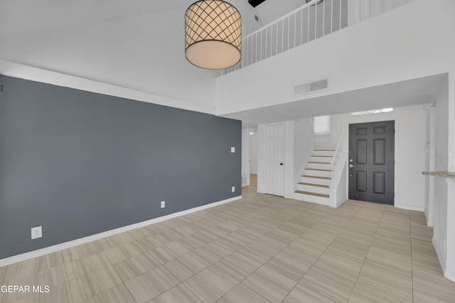 empty room featuring baseboards, stairs, visible vents, and a high ceiling
