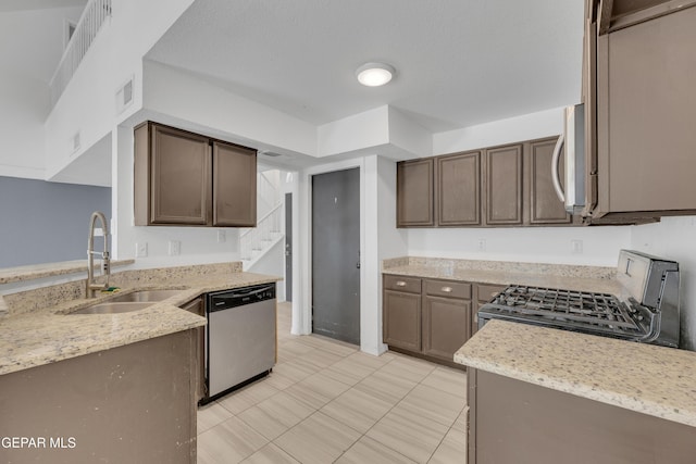 kitchen featuring a sink, stainless steel appliances, dark brown cabinetry, visible vents, and light stone counters