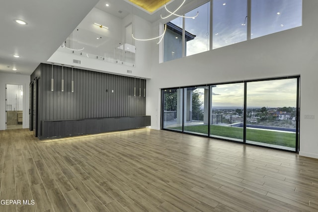 unfurnished living room with visible vents, baseboards, recessed lighting, wood finished floors, and a high ceiling