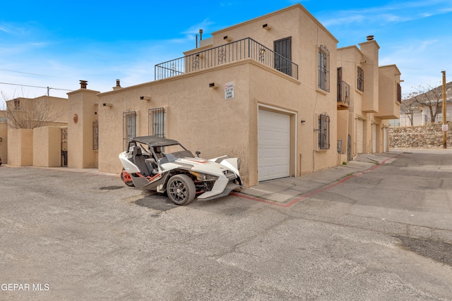 exterior space with an attached garage, stucco siding, and a balcony