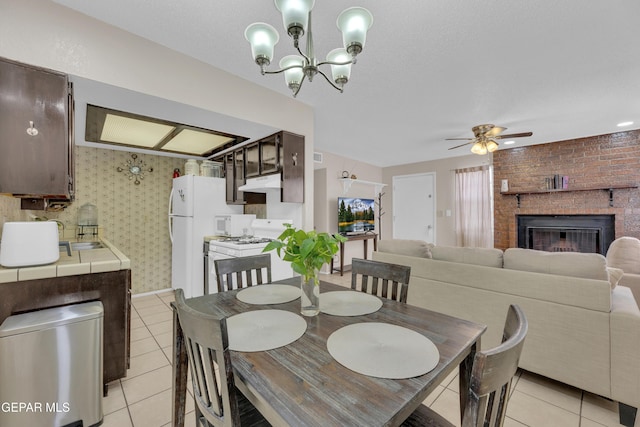 dining area featuring light tile patterned floors, a brick fireplace, and ceiling fan with notable chandelier
