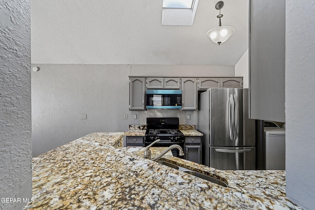 kitchen featuring gray cabinets, stainless steel appliances, a textured wall, a sink, and washer / clothes dryer