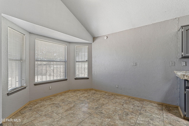 interior space with stone finish floor, baseboards, vaulted ceiling, and plenty of natural light