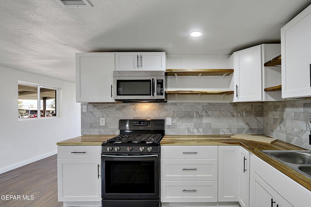 kitchen with range with gas stovetop, stainless steel microwave, open shelves, white cabinetry, and baseboards