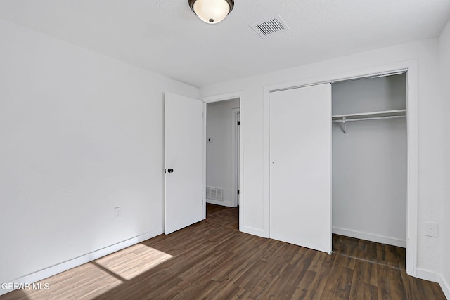 unfurnished bedroom with a closet, visible vents, wood finished floors, and baseboards
