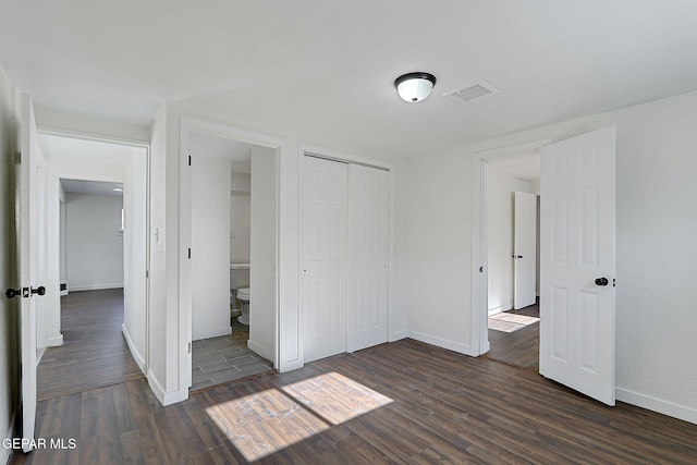 unfurnished bedroom with a closet, visible vents, baseboards, and dark wood finished floors