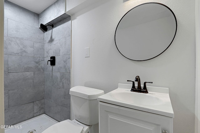 bathroom with a tile shower, toilet, and vanity