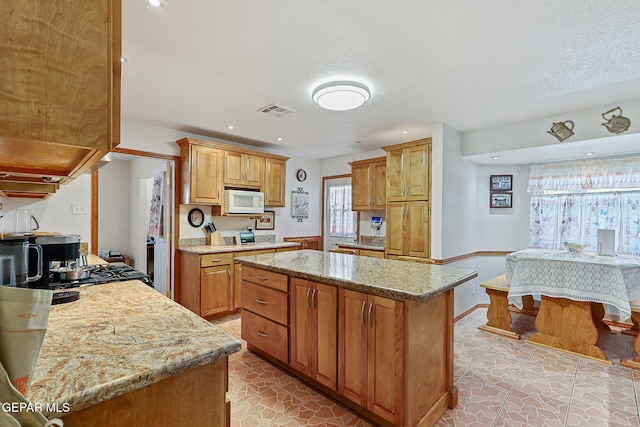 316 Garden Grove Ln, El Paso, TX 79912 - kitchen featuring recessed lighting, light stone countertops, a center island, white microwave, and visible vents