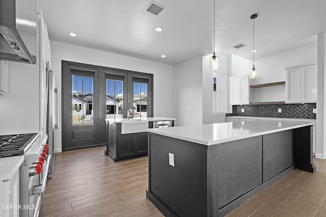 kitchen featuring wall chimney range hood, a center island, double oven range, and a sink