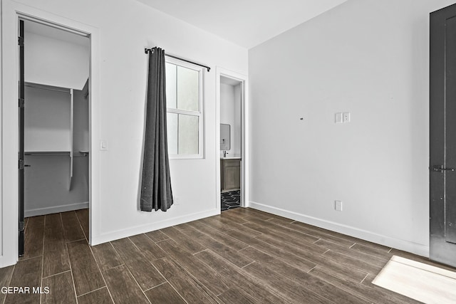 unfurnished bedroom featuring connected bathroom, dark wood-style floors, baseboards, a closet, and a spacious closet