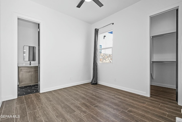 unfurnished bedroom with a walk in closet, ensuite bath, dark wood-style floors, and baseboards
