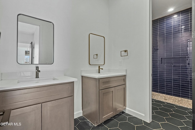 full bath featuring a tile shower, two vanities, a sink, and baseboards