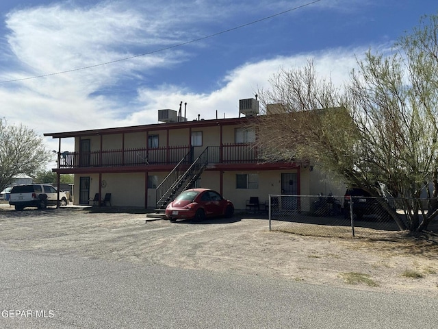 view of building exterior with fence, stairway, uncovered parking, and central air condition unit