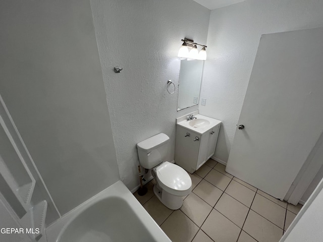 bathroom featuring tile patterned flooring, a tub to relax in, toilet, a textured wall, and vanity